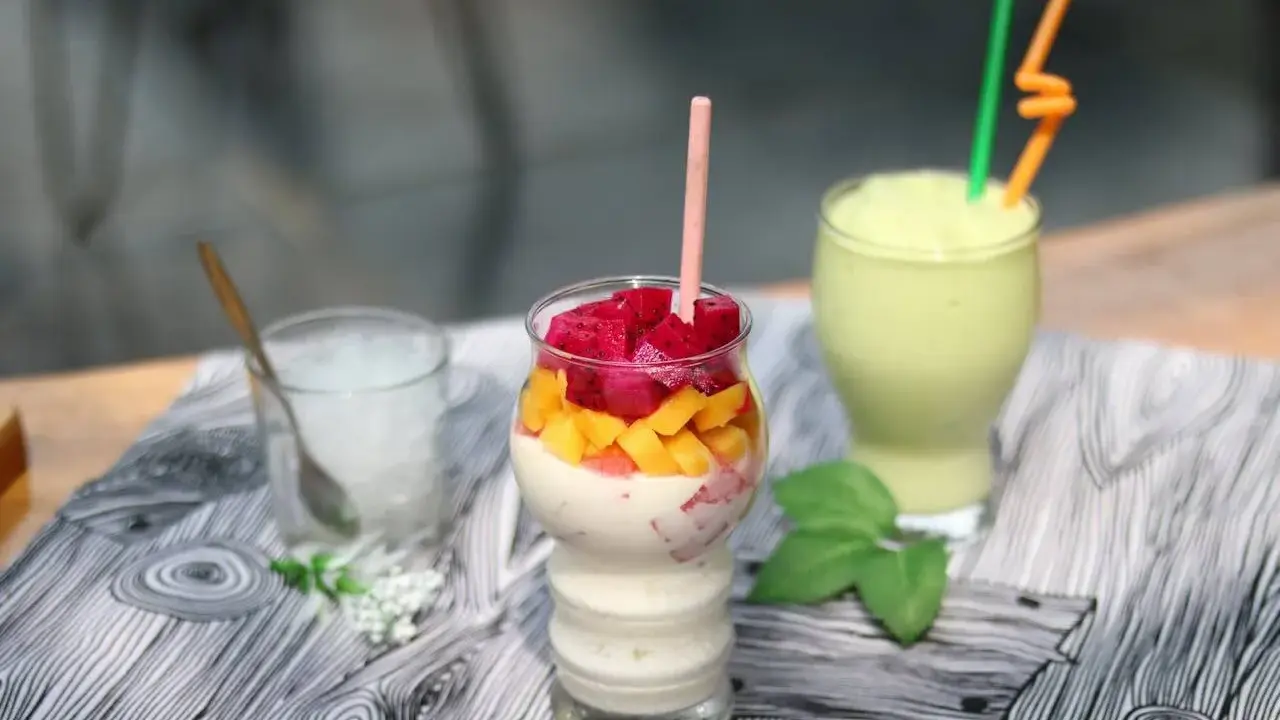 Pyszny koktajl białkowy z kawałkami smoczego owocu i mango. Obok zielony smoothie i szklanka z lodem.