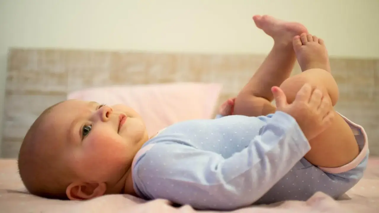 5-miesięczne dziecko leży na plecach, podnosząc nóżki i bawiąc się nimi. To pokazuje, co potrafi 5 miesięczne dziecko.