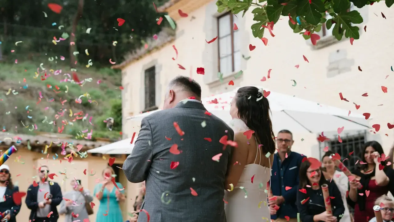 Novios bajo una lluvia de confeti en forma de corazón. Los invitados lanzan confeti, creando un ambiente festivo, perfecto para las canciones de boda.