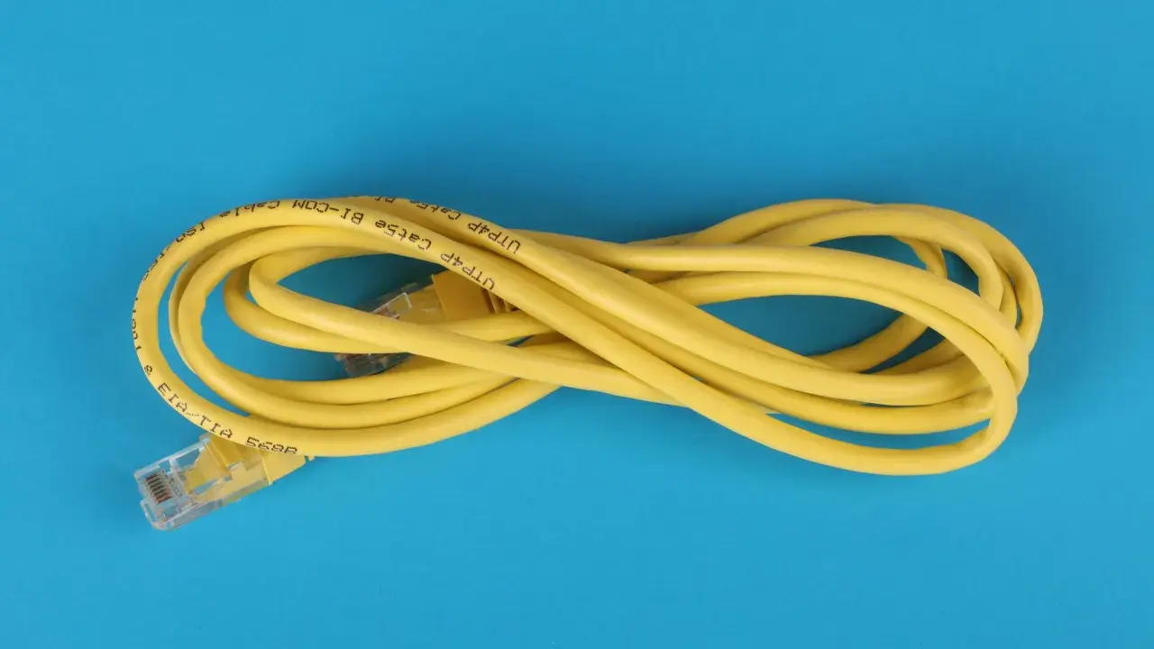 Un câble Ethernet jaune enroulé sur fond bleu. Il est marqué "UTP Cat5e BI-COM". Un bon choix pour votre réseau.