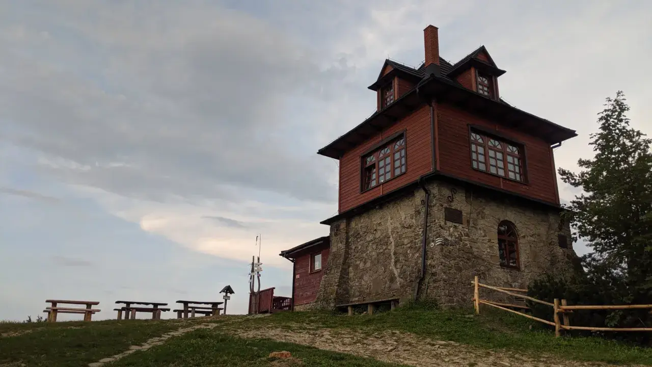 Drewniana wieża widokowa na Luboniu Wielkim, z kamiennym fundamentem, otoczona zielenią i ławkami.