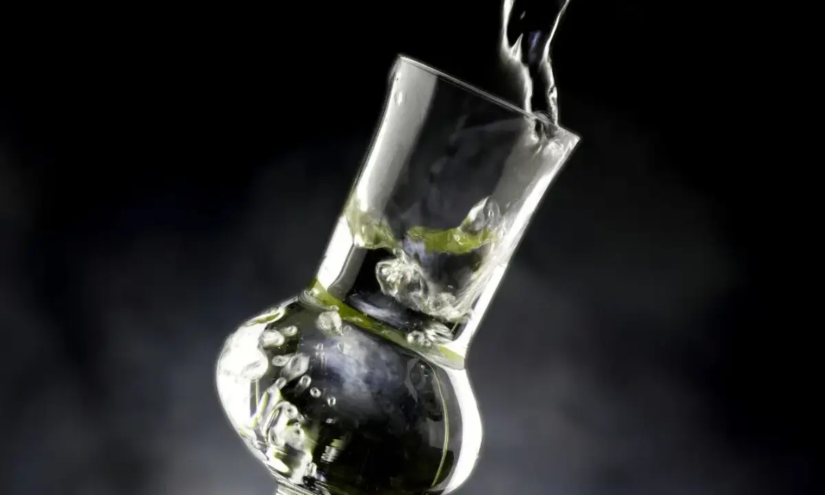 Klarer Grappa wird in ein Glas gegossen. Die Frage "wie viel prozent hat grappa" wird durch die klare Flüssigkeit und die Bläschen im Glas angedeutet.