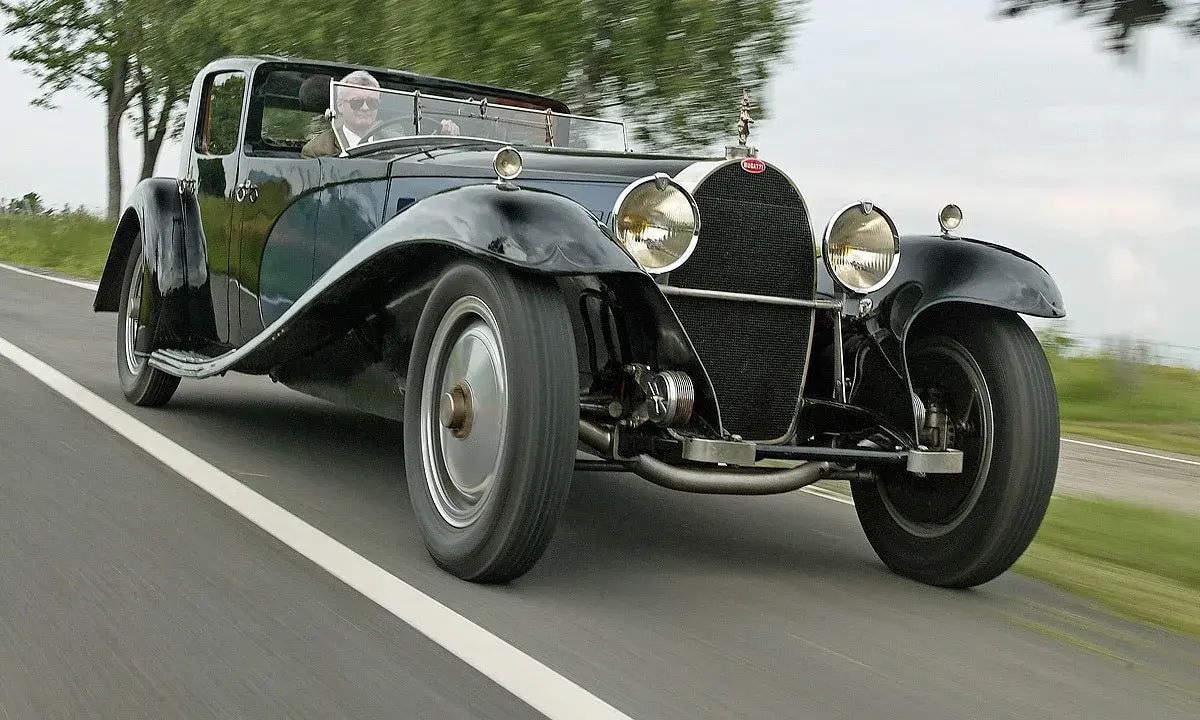 Ein Mann fährt einen glänzenden schwarzen Bugatti Royale auf einer Landstraße. Der Bugatti Royale Preis ist astronomisch, ein Traum für jeden Sammler.