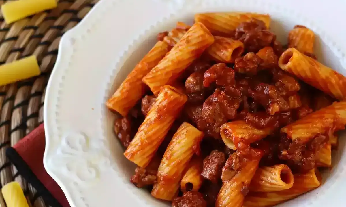 En portion pasta med korv i tomatsås, serverad på en vit tallrik.