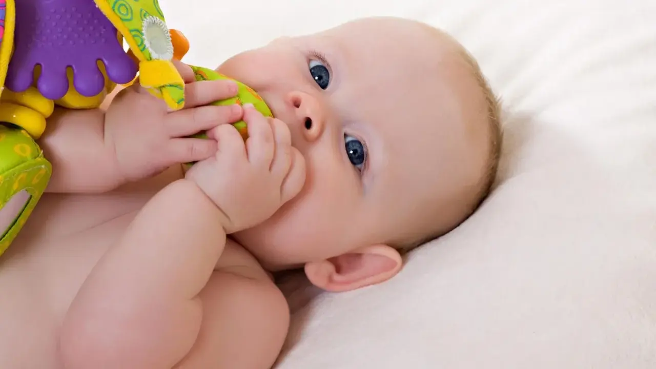 Ein Baby mit blauen Augen erkundet sein buntes Spielzeug. Vielleicht ist es der 19-Wochen-Schub, der ihn so neugierig macht.