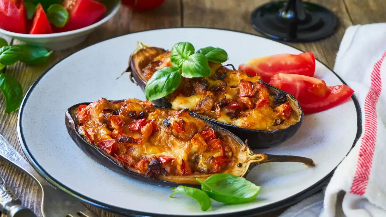 Melanzane ripiene senza carne, dorate e filanti, guarnite con basilico fresco e pomodoro. Un piatto vegetariano invitante.