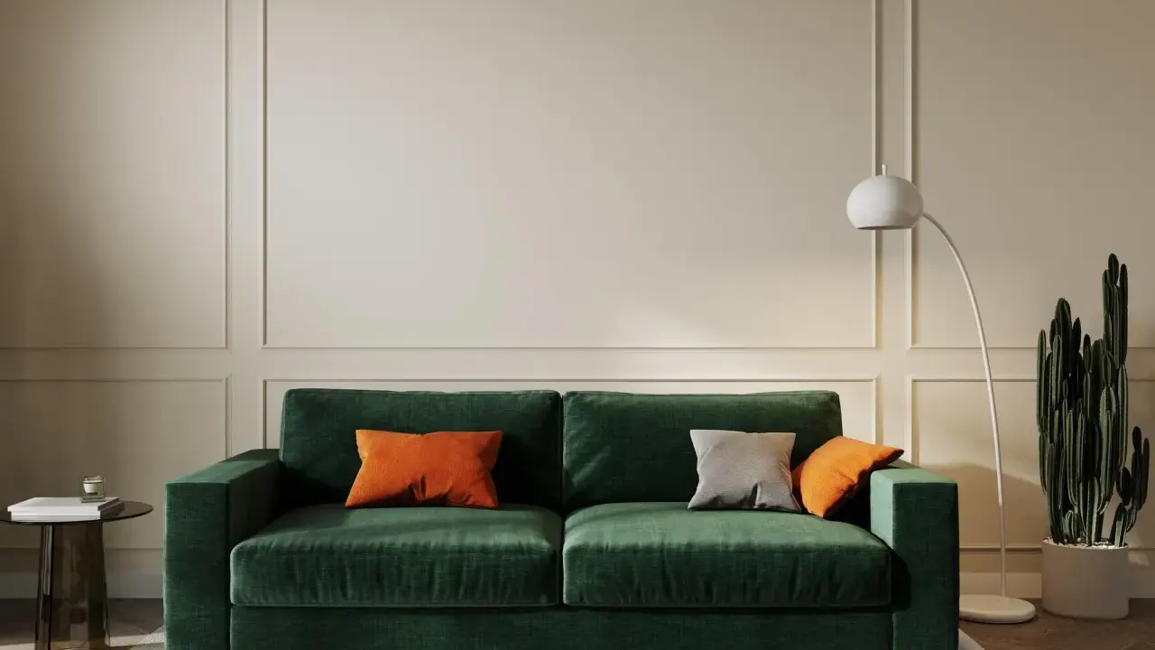 Elegancki salon w odcieniach butelkowej zieleni i beżu. Miękka sofa, nowoczesna lampa i kaktus tworzą przytulną atmosferę.