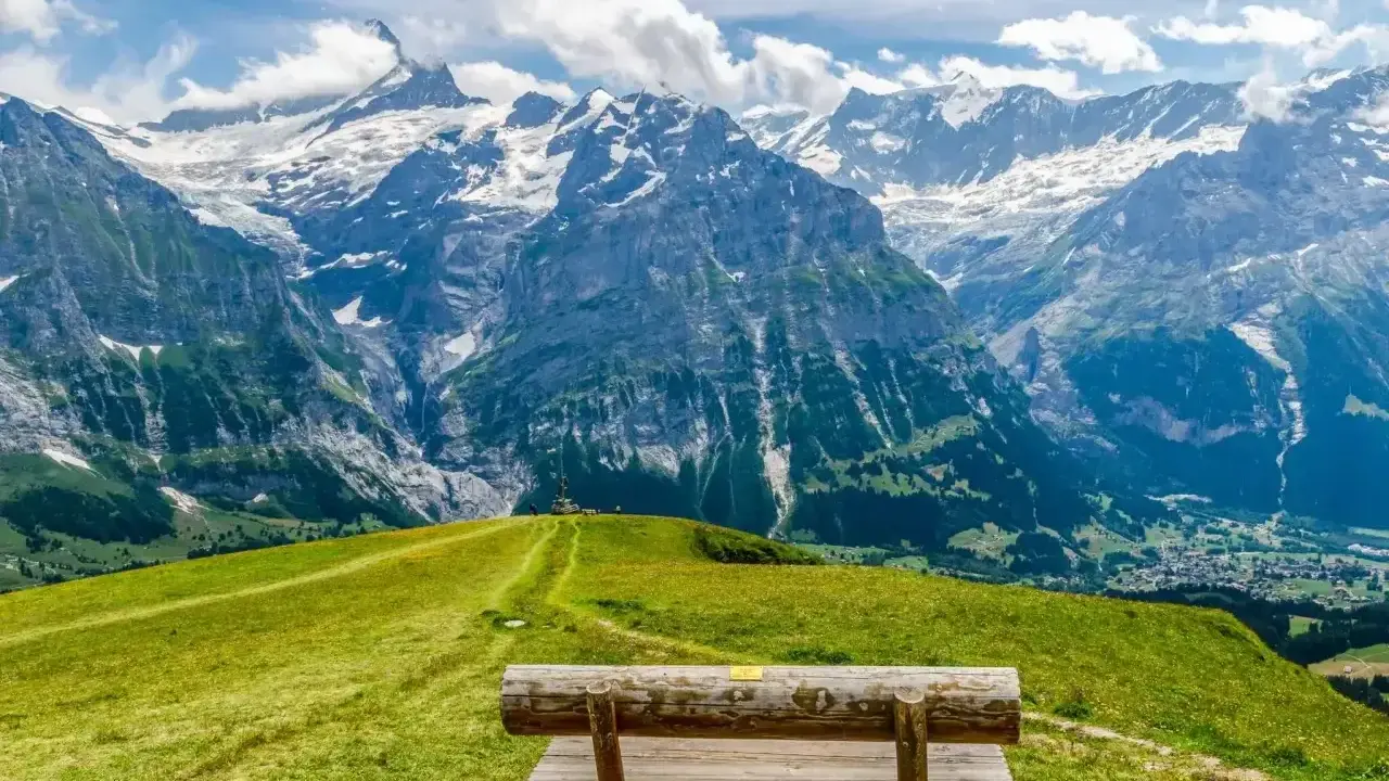 Ławka na tle majestatycznych gór w Grindelwald. Zielone wzgórza i skaliste szczyty tworzą zapierający dech w piersiach krajobraz.