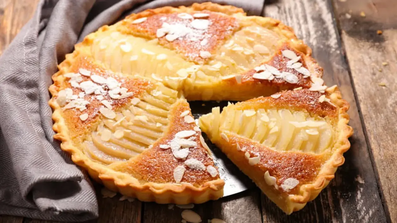 Une délicieuse tarte aux poires, garnie d'amandes effilées et saupoudrée de sucre glace, repose sur un plateau en bois.