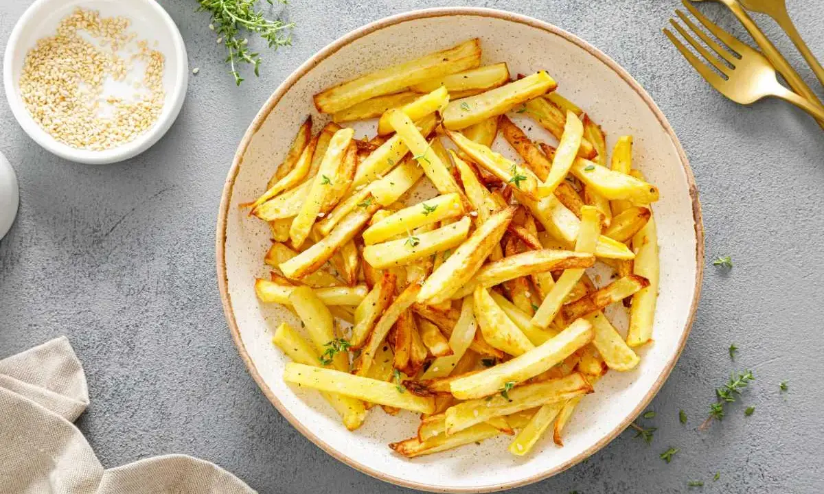 Un plato lleno de crujientes patatas fritas doradas, espolvoreadas con hierbas frescas. ¡Perfectas para compartir!