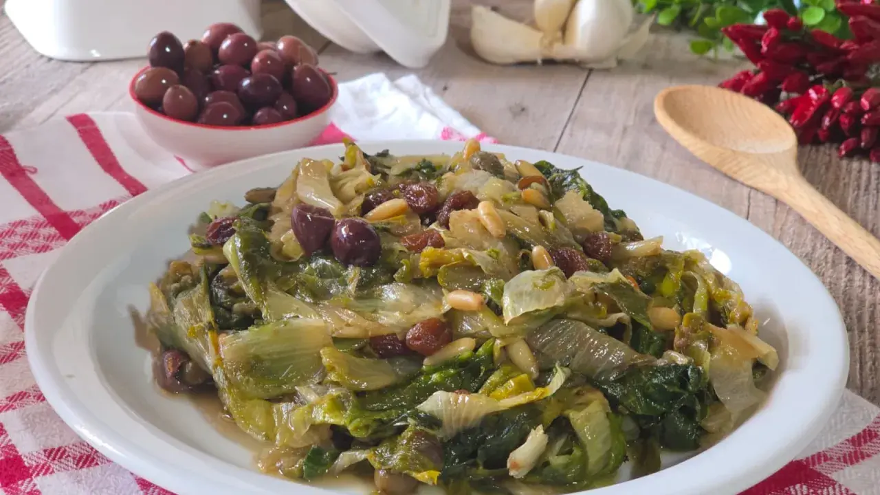 Scarola in padella con olive, pinoli e uvetta, un contorno saporito e colorato.