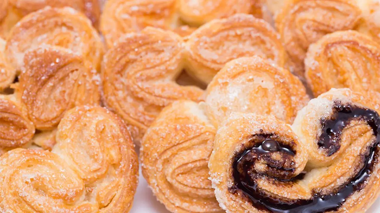 Deliciosas palmeritas de hojaldre espolvoreadas con azúcar. Algunas tienen un relleno de chocolate oscuro y brillante.