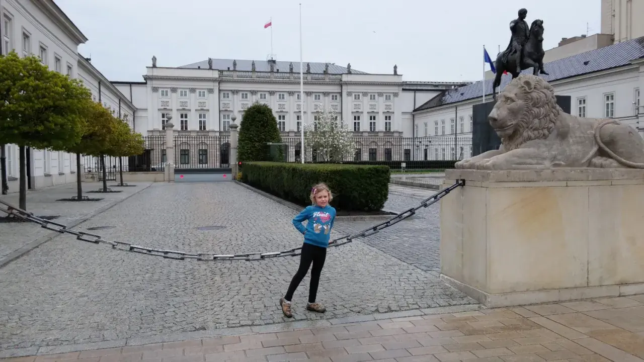Dziewczynka na trasie traktu królewskiego w Warszawie, obok lwa i pomnika konnego.