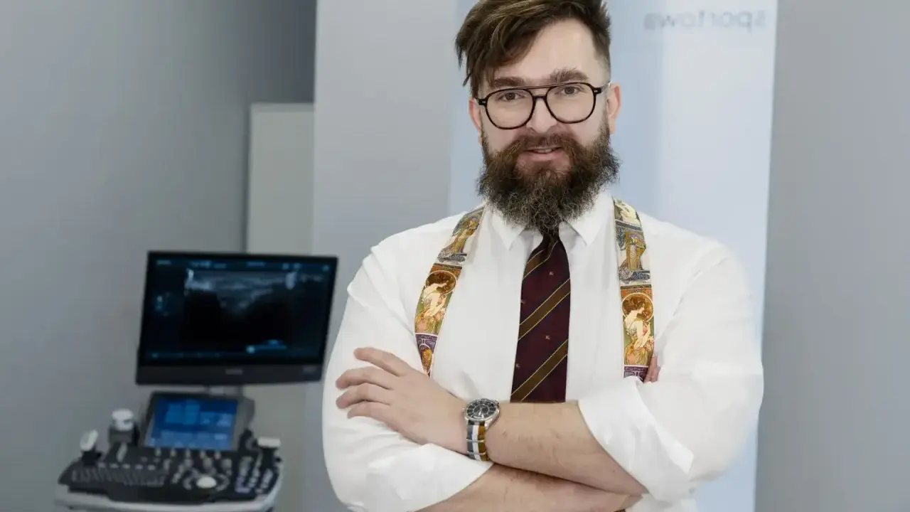 Ortopeda w okularach i ozdobnych szelkach stoi przed aparatem USG.