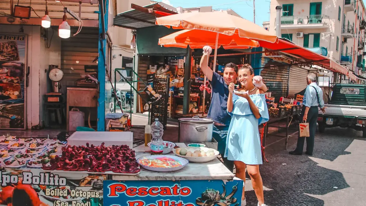 Coppia felice assaggia polpo fritto in un mercato di Palermo in un giorno di sole. Un assaggio autentico della Sicilia.