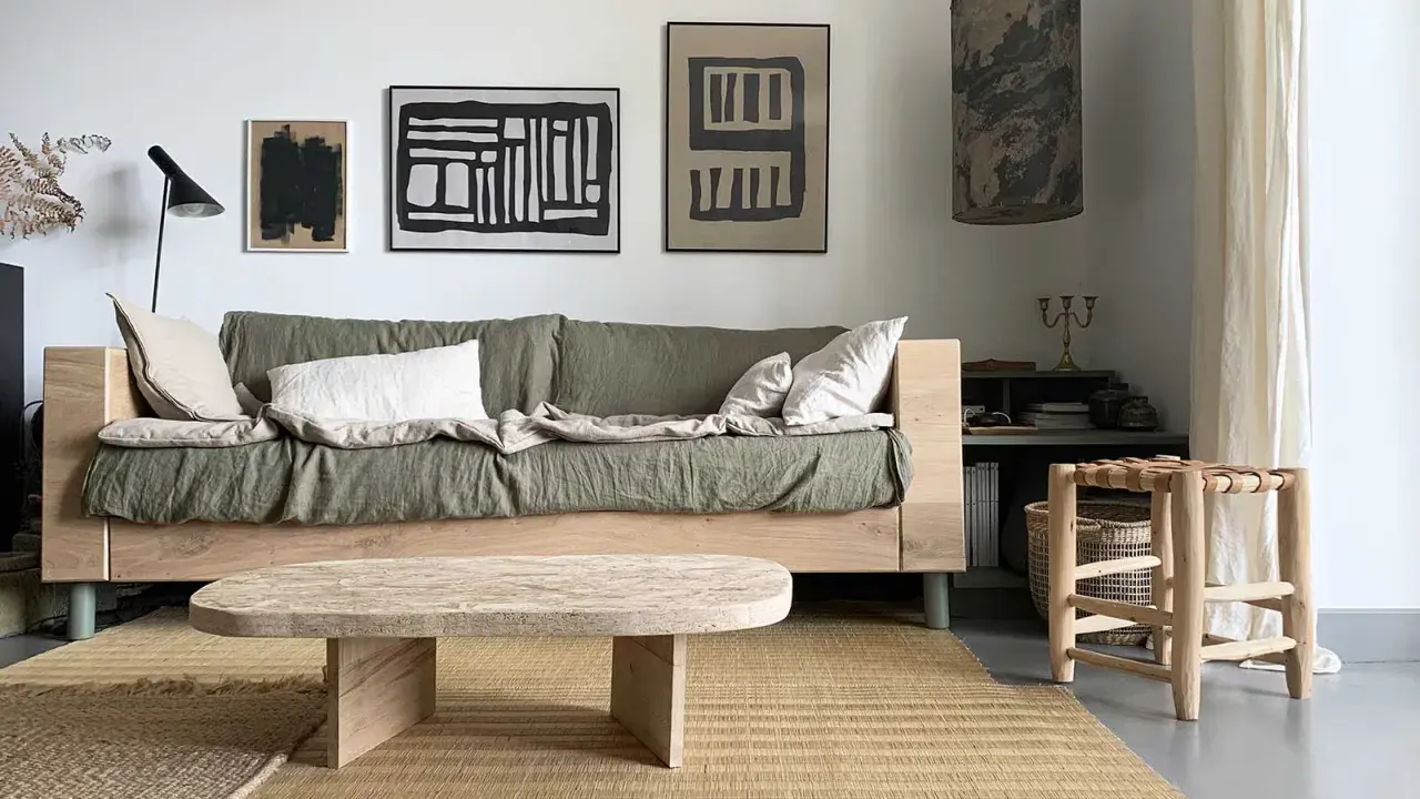 Une idée table basse fait maison en bois brut, posée sur un tapis tressé, devant un canapé vert et des tableaux abstraits.