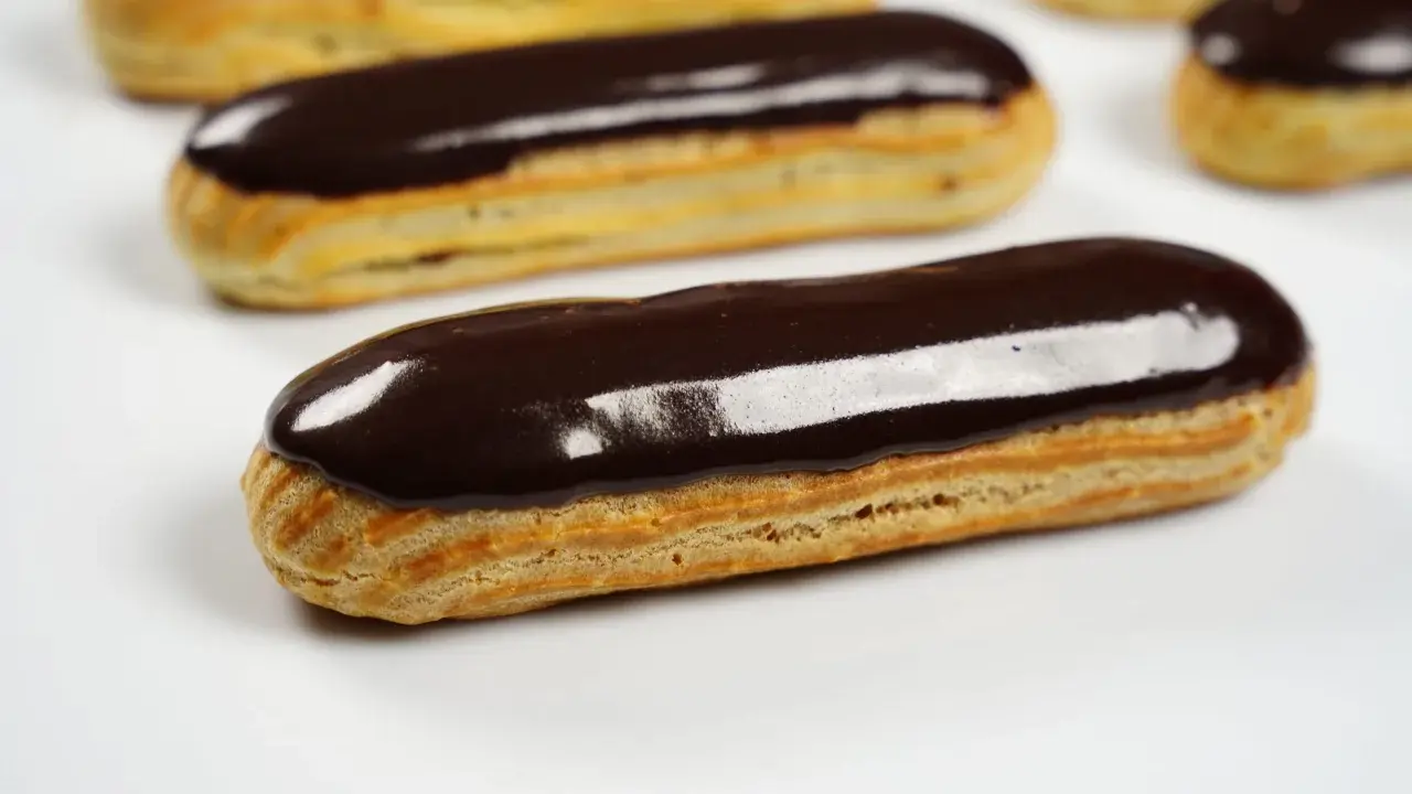 Plusieurs éclairs au chocolat brillants, avec un fondant pour éclair parfait, sont disposés sur fond blanc.