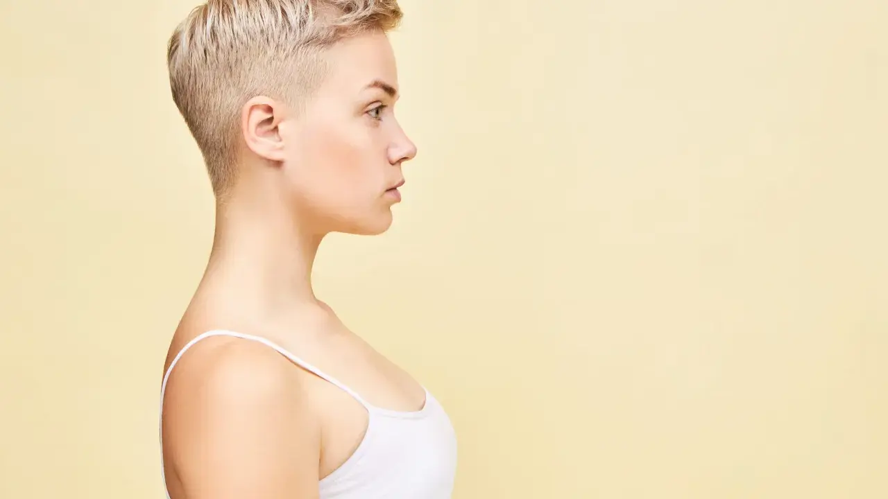 Perfil de una mujer joven con un moderno corte pixie rubio, luciendo un top blanco.