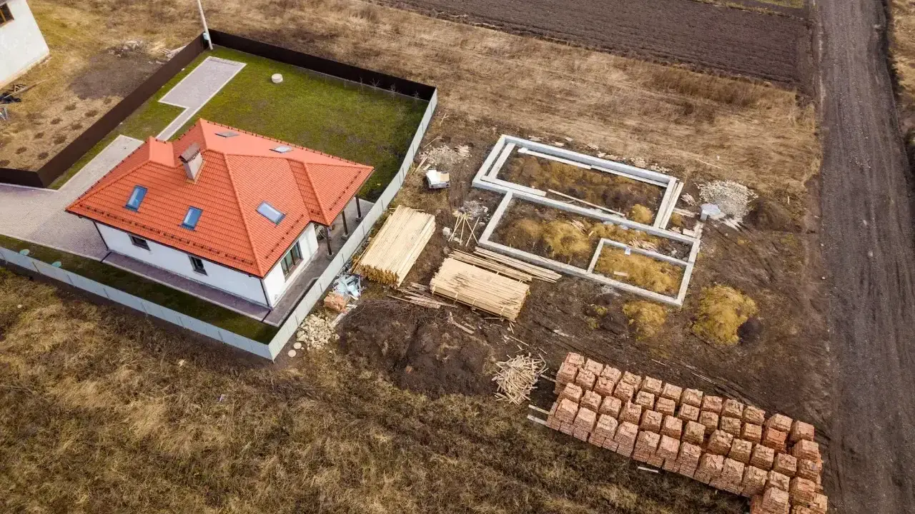 Działka rolno budowlana z gotowym domem i fundamentami pod kolejny. Materiały budowlane czekają na rozpoczęcie prac.