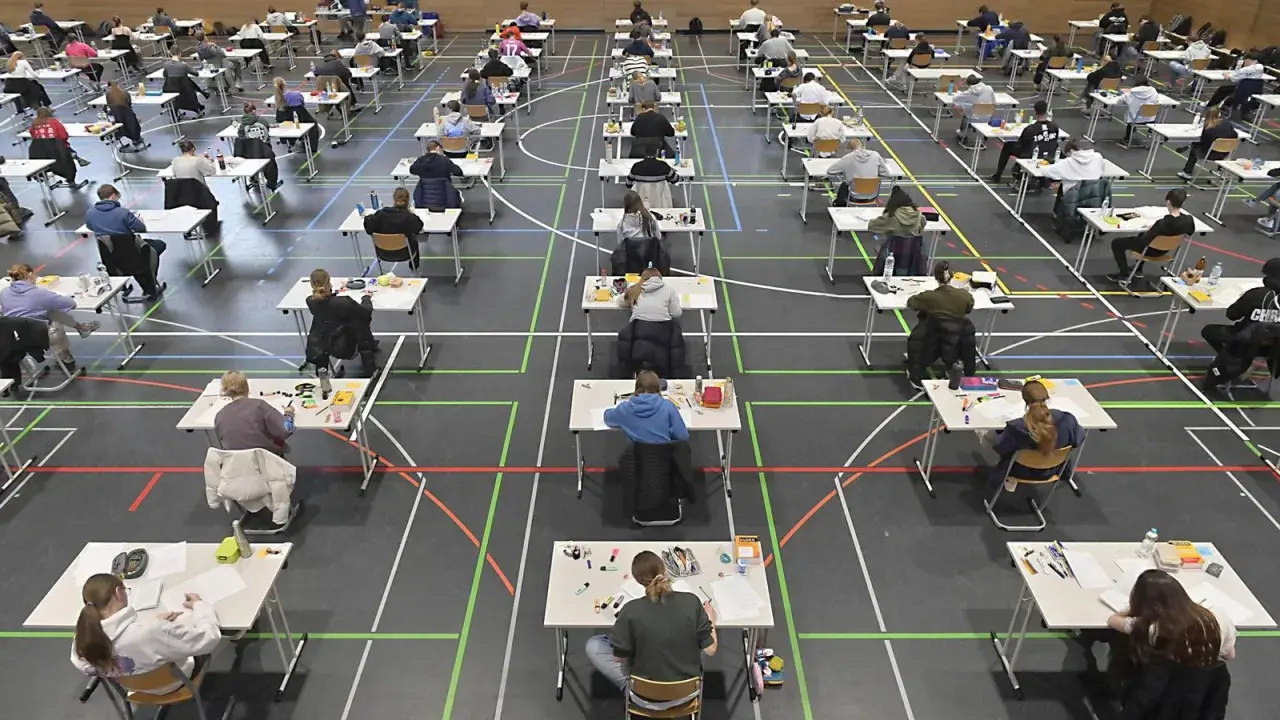 Viele Schüler sitzen in einer Sporthalle an Tischen, um zum Abitur zu schreiben.