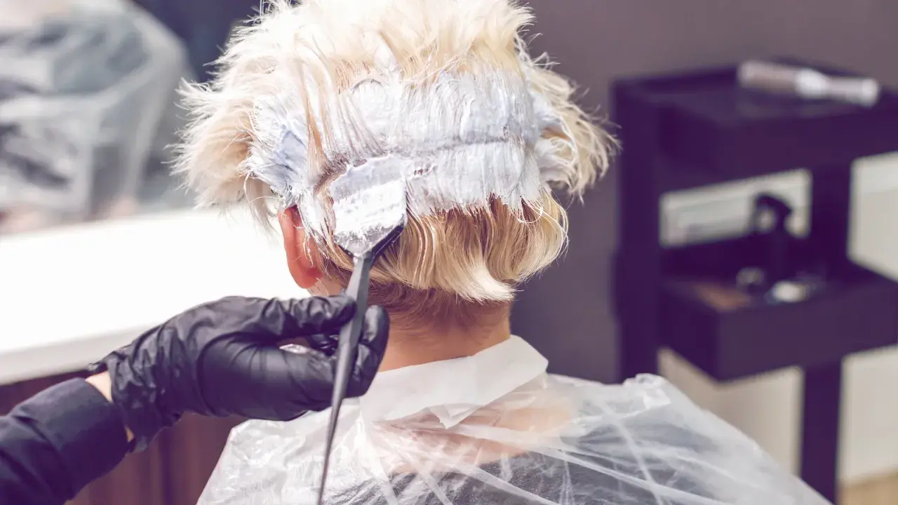 Friseur mit Handschuhen trägt Bleichmittel auf blondes Haar auf. Der Prozess des Haare bleichen beginnt.