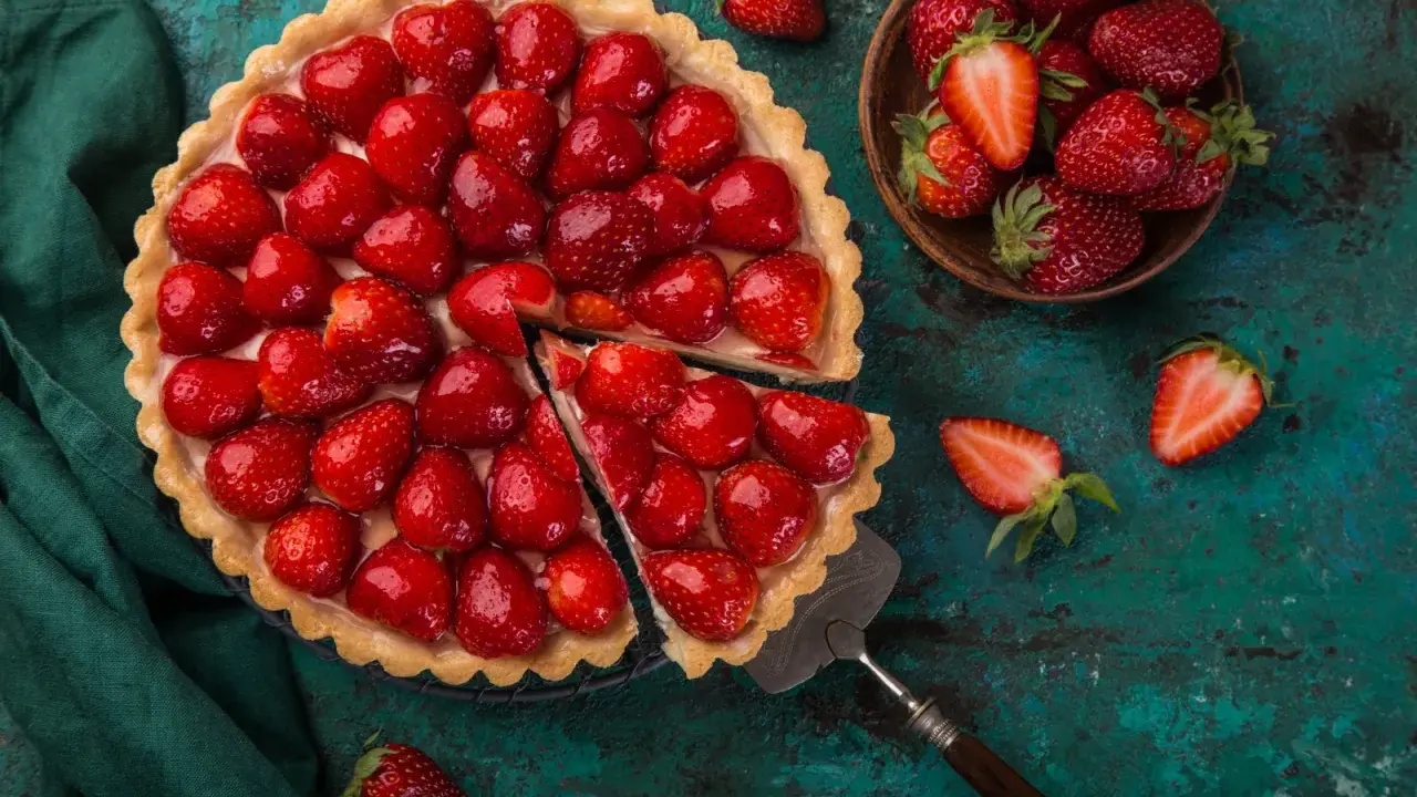 Une magnifique tarte aux fraises, garnie de fruits rouges brillants, est prête à être dégustée. Une part a été coupée, révélant la crème onctueuse.