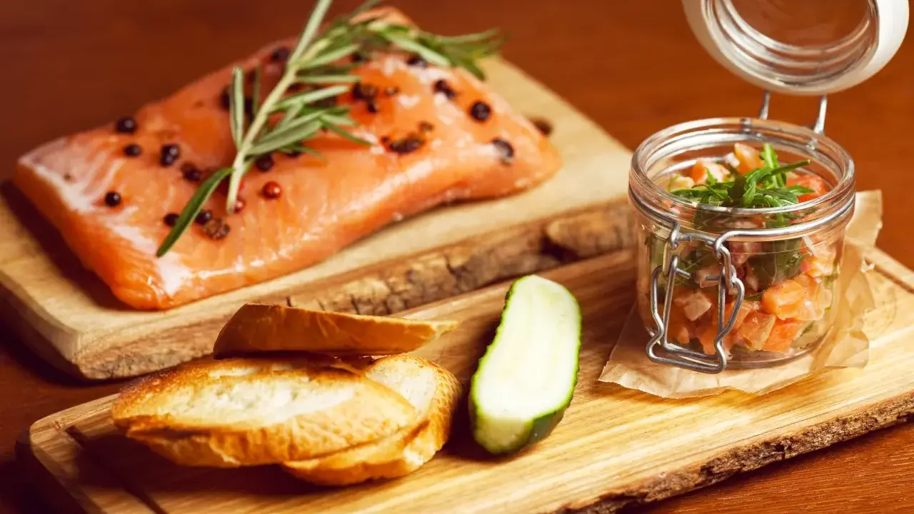 Świeży łosoś z rozmarynem i pieprzem, tartare w słoiczku, pieczywo i ogórek. Zdrowe łosoś kcal na drewnianej desce.