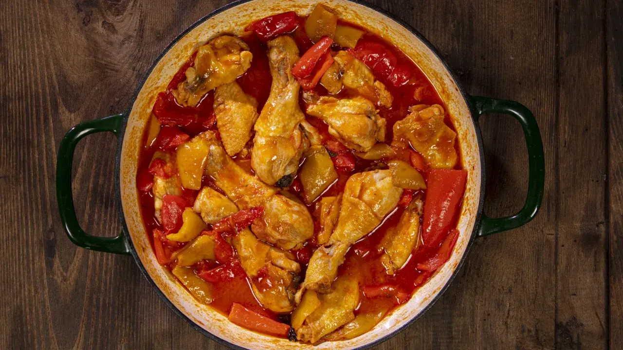 Un saporito pollo con peperoni in umido, cotto in una casseruola verde su un tavolo di legno scuro.