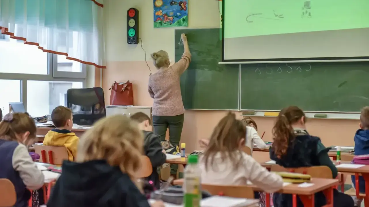 Nauczycielka dyplomowana pisze na tablicy, dzieci słuchają. Ciekawe, jakie nauczyciel dyplomowany zarobki ma w tej szkole.