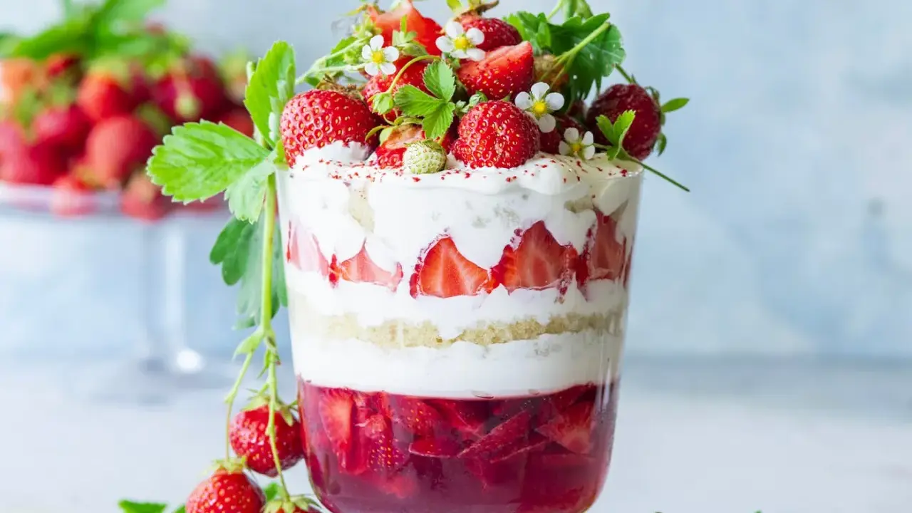 Verrine fraise fromage blanc, un délice estival en couches de génoise, crème et fruits rouges frais, décorée de fraises et de fleurs.