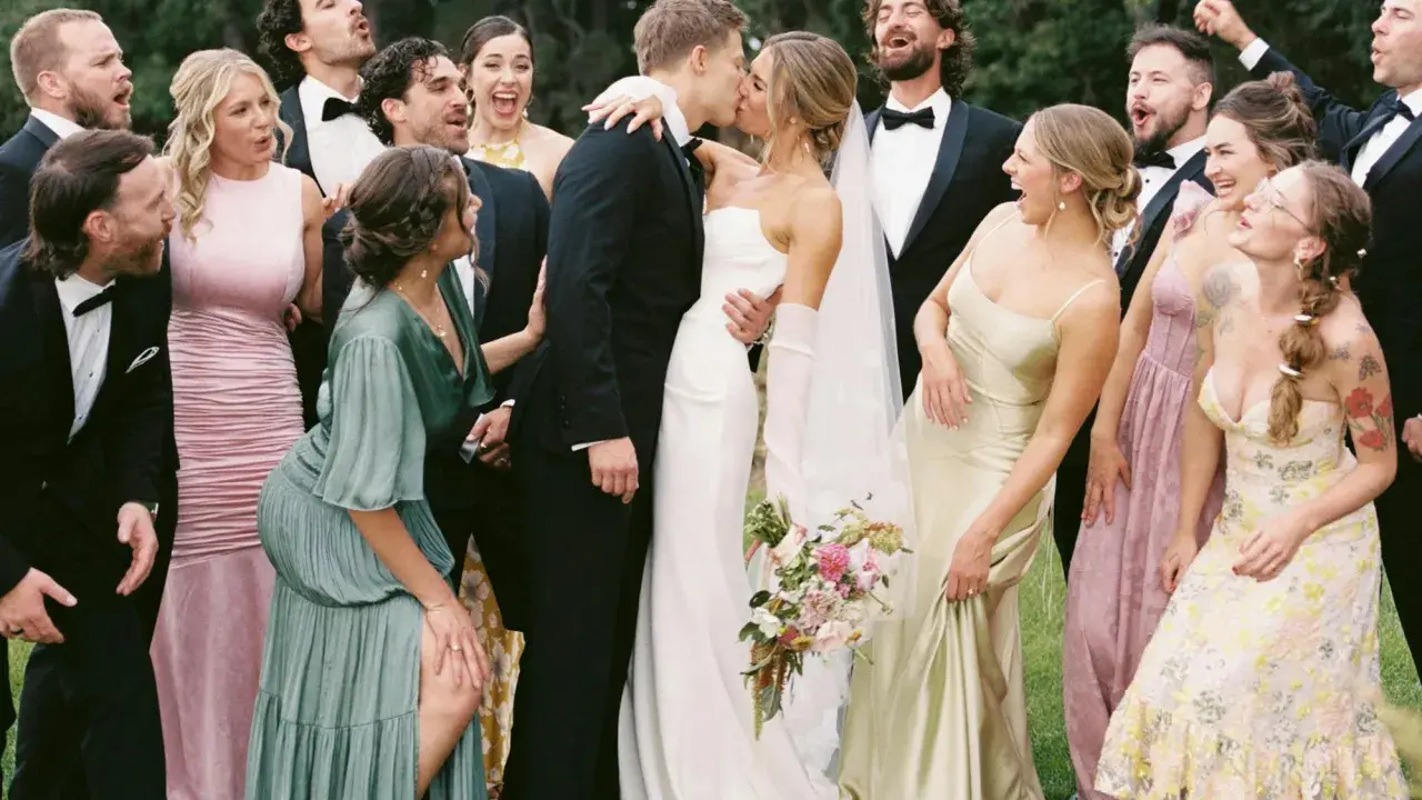 A wedding party celebrates as the bride and groom kiss. The groomsmen attire is classic black tuxedos.