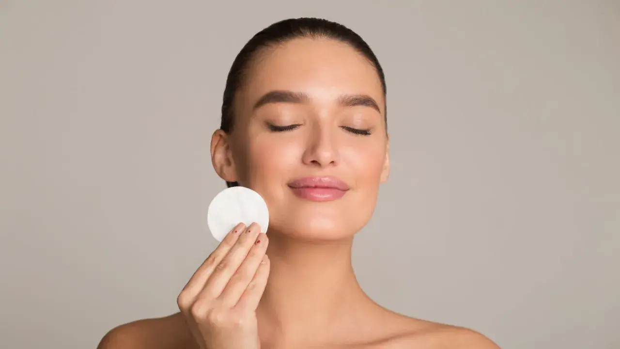 Donna con occhi chiusi applica un dischetto di cotone sul viso, parte della sua routine di skincare viso per una pelle radiosa.