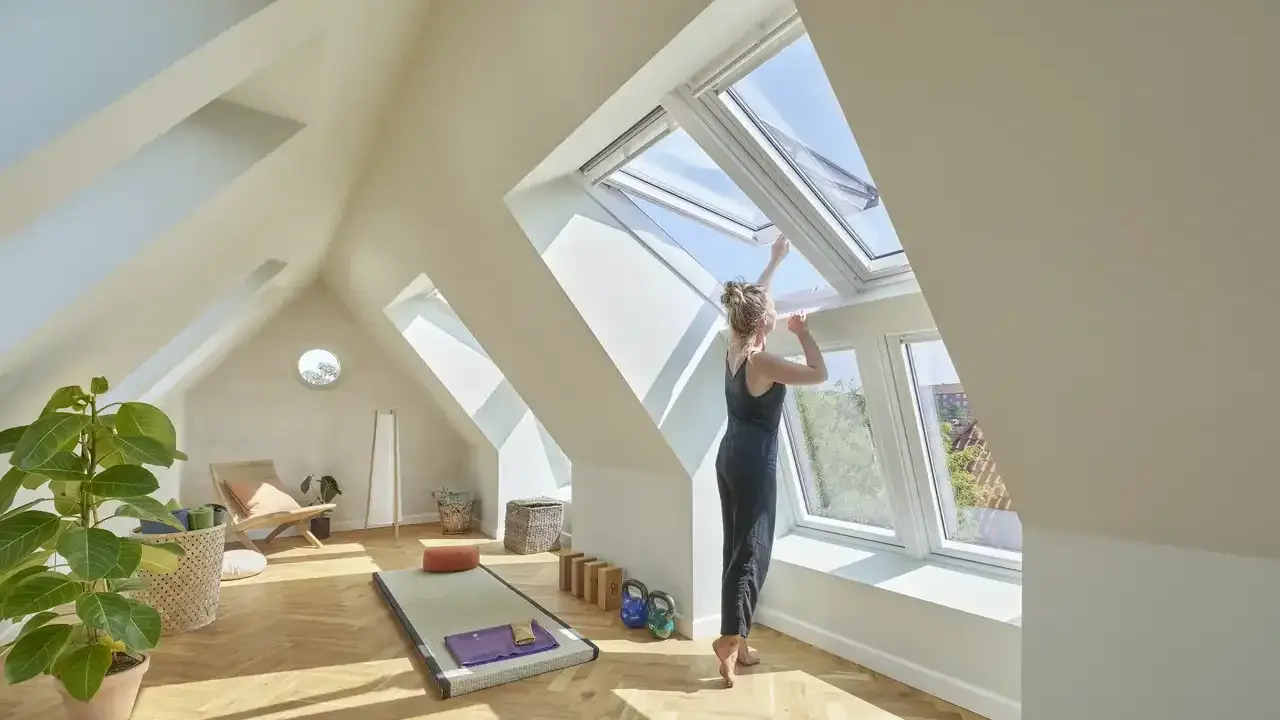 Frau öffnet Dachfenster in hellem Dachboden-Yoga-Raum. Hier darf man Dachboden als Wohnraum nutzen und schafft sich eine Oase.