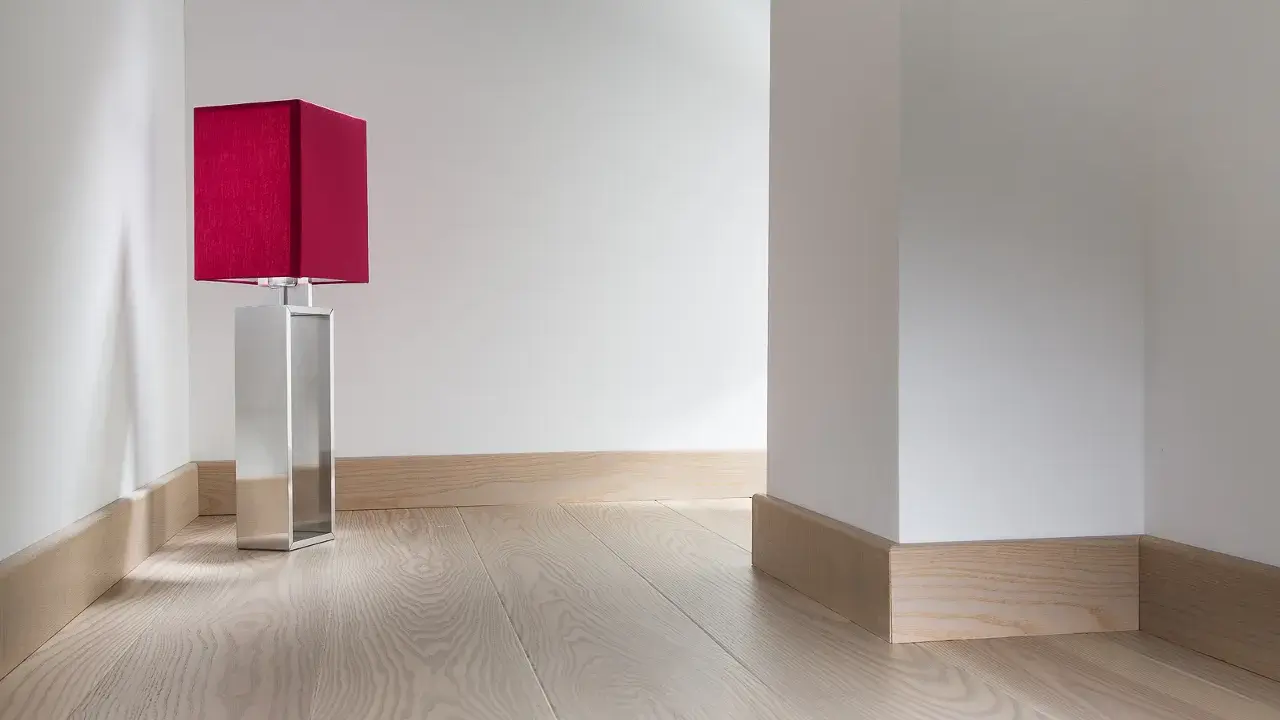 Enkel golvlistsinspiration i ljust trä som ramar in ett modernt rum med en röd bordslampa.