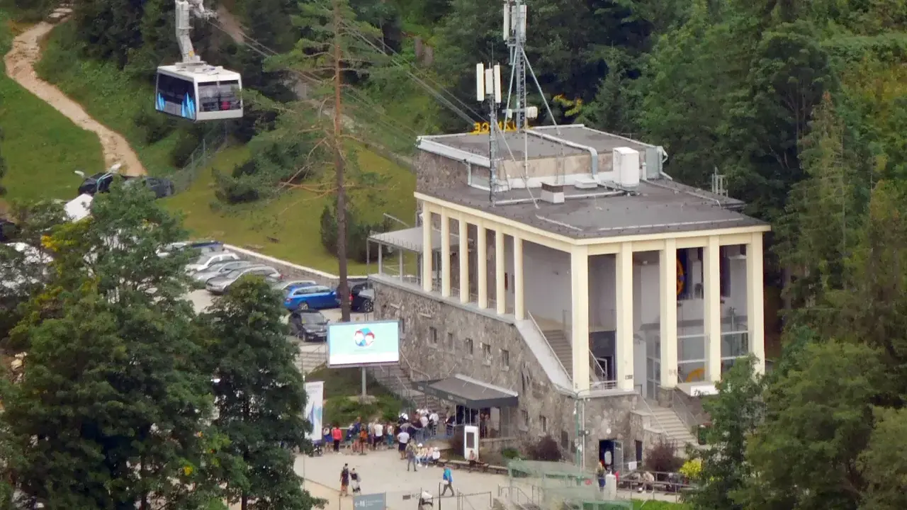 Kolejka linowa nad budynkiem stacji PKL na Kasprowym Wierchu, z widocznymi samochodami i ludźmi.