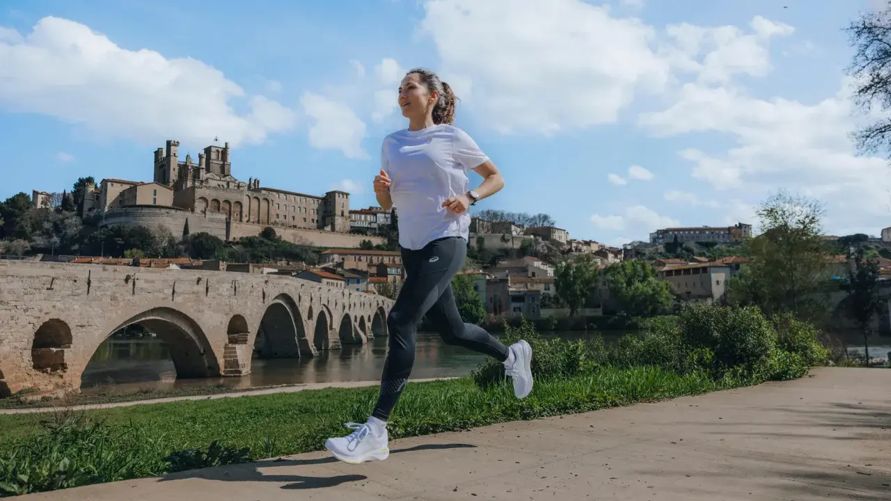 Kobieta biegnie wzdłuż rzeki, mijając zabytkowy most i miasto. Zastanawia się, ile się biegnie 5 km.