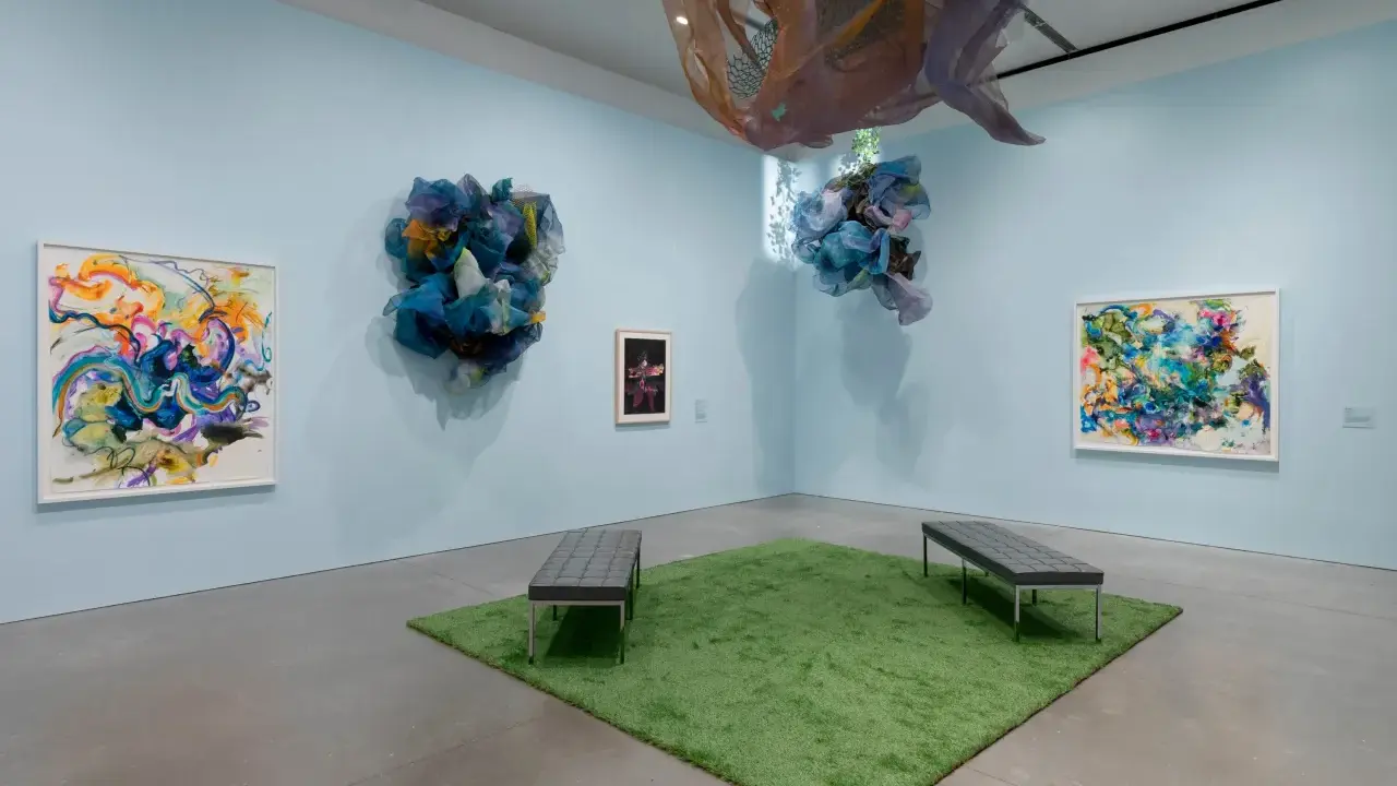 Abstract paintings and fabric sculptures adorn the walls of the Lanoue Gallery, with benches placed on a patch of artificial grass.