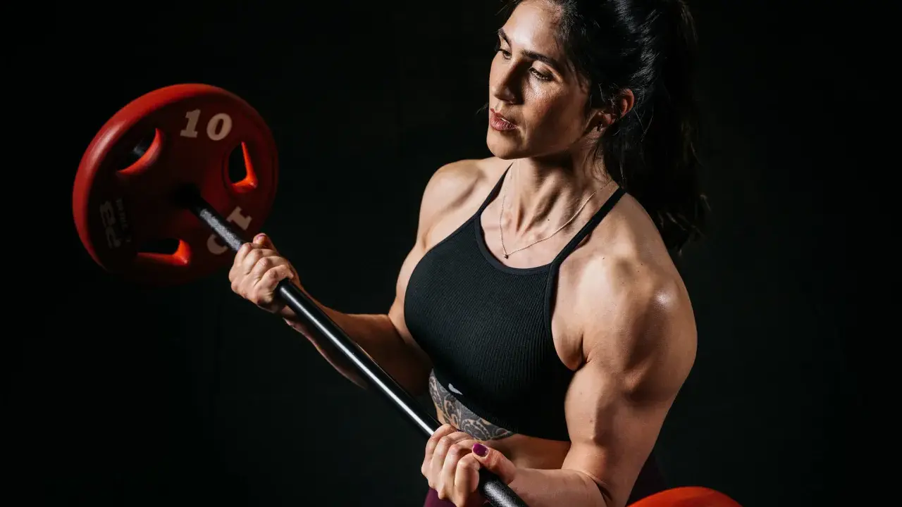 Eine starke Bodybuilderin Frau hebt eine Hantel. Ihre Muskeln sind deutlich sichtbar.