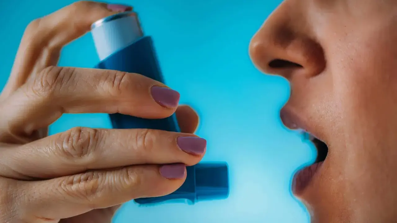 Person nutzt Asthmaspray vor oder nach dem Sport. Die Hand hält das blaue Gerät, der Mund ist geöffnet.