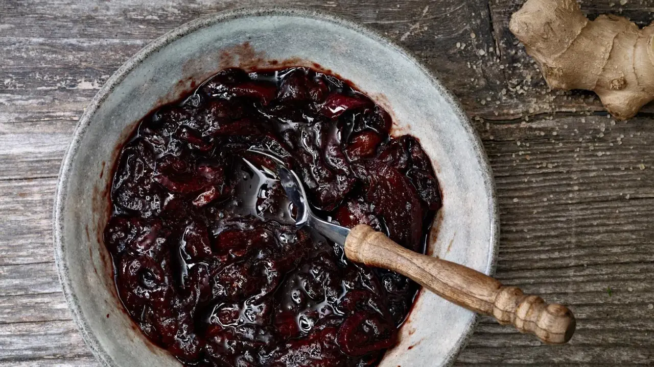Dunkles, glänzendes Zwetschgen-Chutney in einer Schale, daneben ein Stück Ingwer und Zucker.