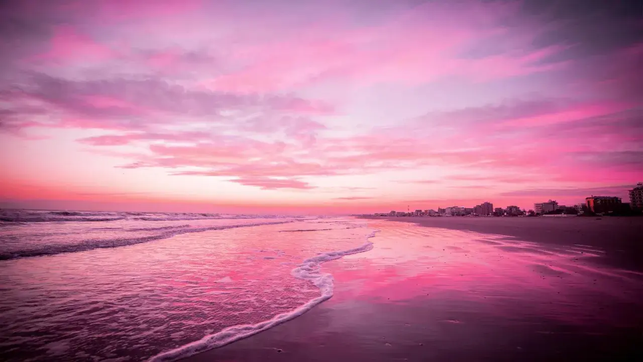 Spiaggia di Riccione immersa nel rosa della Notte Rosa, con il mare calmo e il cielo infuocato.