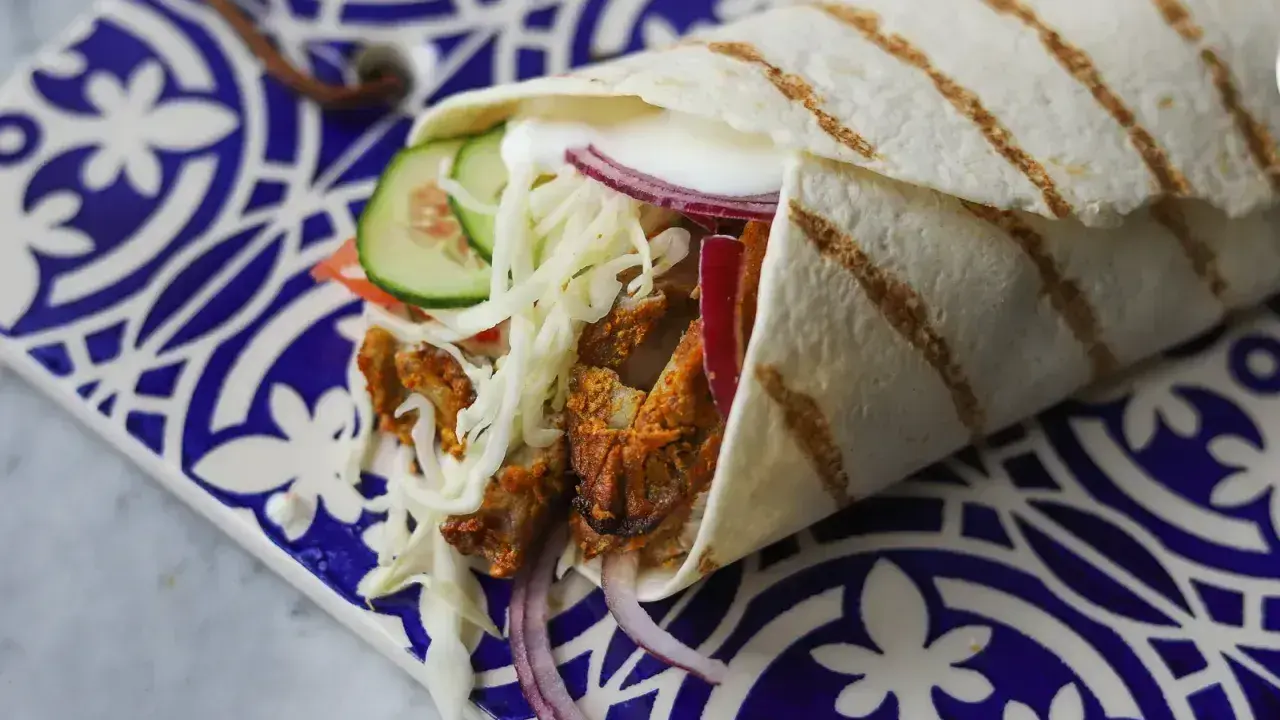 Pyszny kebab w picie z soczystym mięsem, chrupiącą kapustą, pomidorem, ogórkiem i czerwoną cebulą, podany na ozdobnym talerzu.