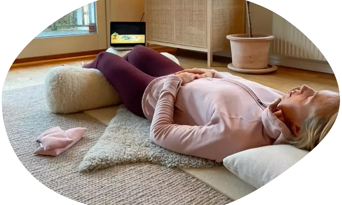 Kvinna ligger på rygg på en matta med en kudde under knäna, hon försöker varva ner med en laptop i bakgrunden.