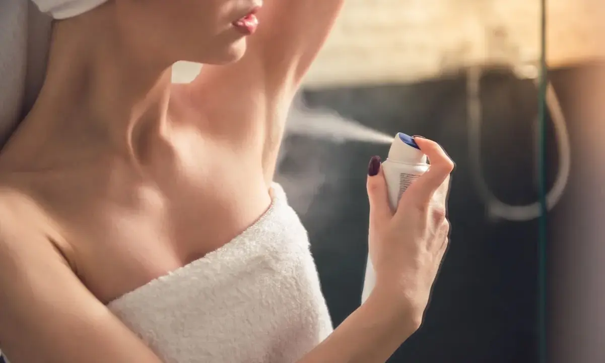 Kobieta aplikuje antyperspirant pod pachę, pokazując różnicę między dezodorantem a antyperspirantem.