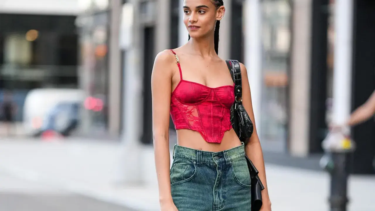 Frau mit geflochtenen conros Haare trägt ein rotes Korsett-Top und Jeans.