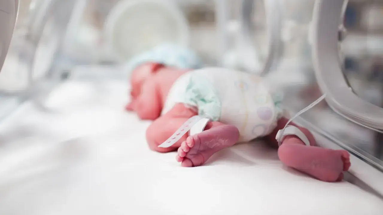 Un bebé prematuro duerme en una incubadora de bebés, con pulseras de identificación en sus tobillos.