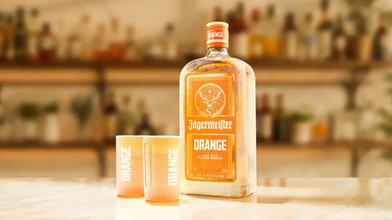 Butelka Jägermeister Orange i dwa kieliszki z napisem "ORANGE" na blacie. Idealny zestaw na letnie wieczory.