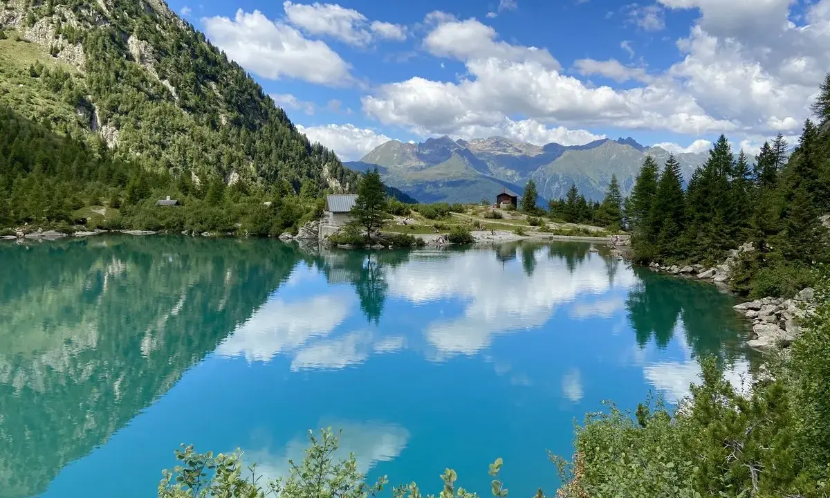 Lago alpino cristallino, perfetto per passeggiate in montagna Lombardia. Riflessi di cielo e montagne.