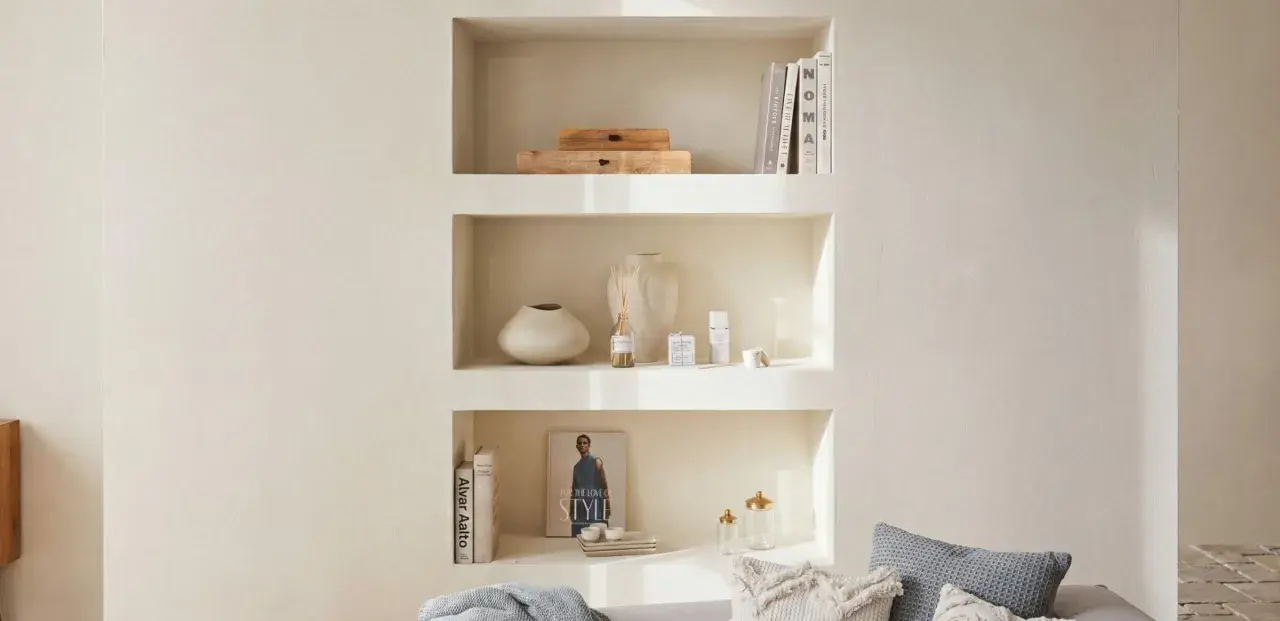Una nicchia nel muro del salotto, con libri, vasi e diffusore, crea un angolo accogliente e ordinato.