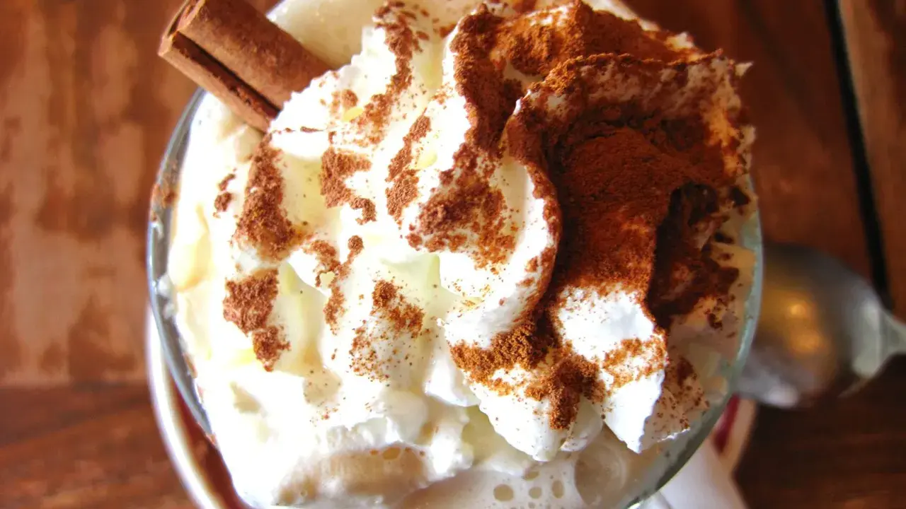 Un déliceux café liégeois recette : crème fouettée, cacao et bâton de cannelle dans un verre.